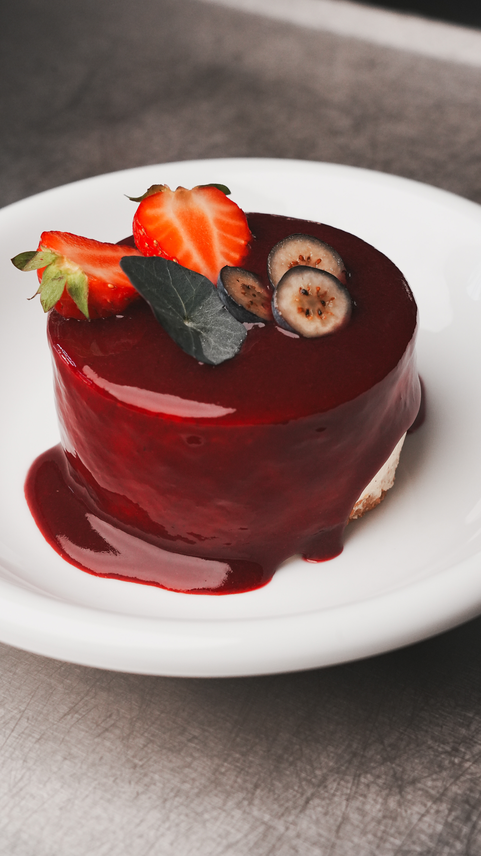Dessert glacé rouge garni de fraises, myrtilles et feuille verte sur assiette blanche.