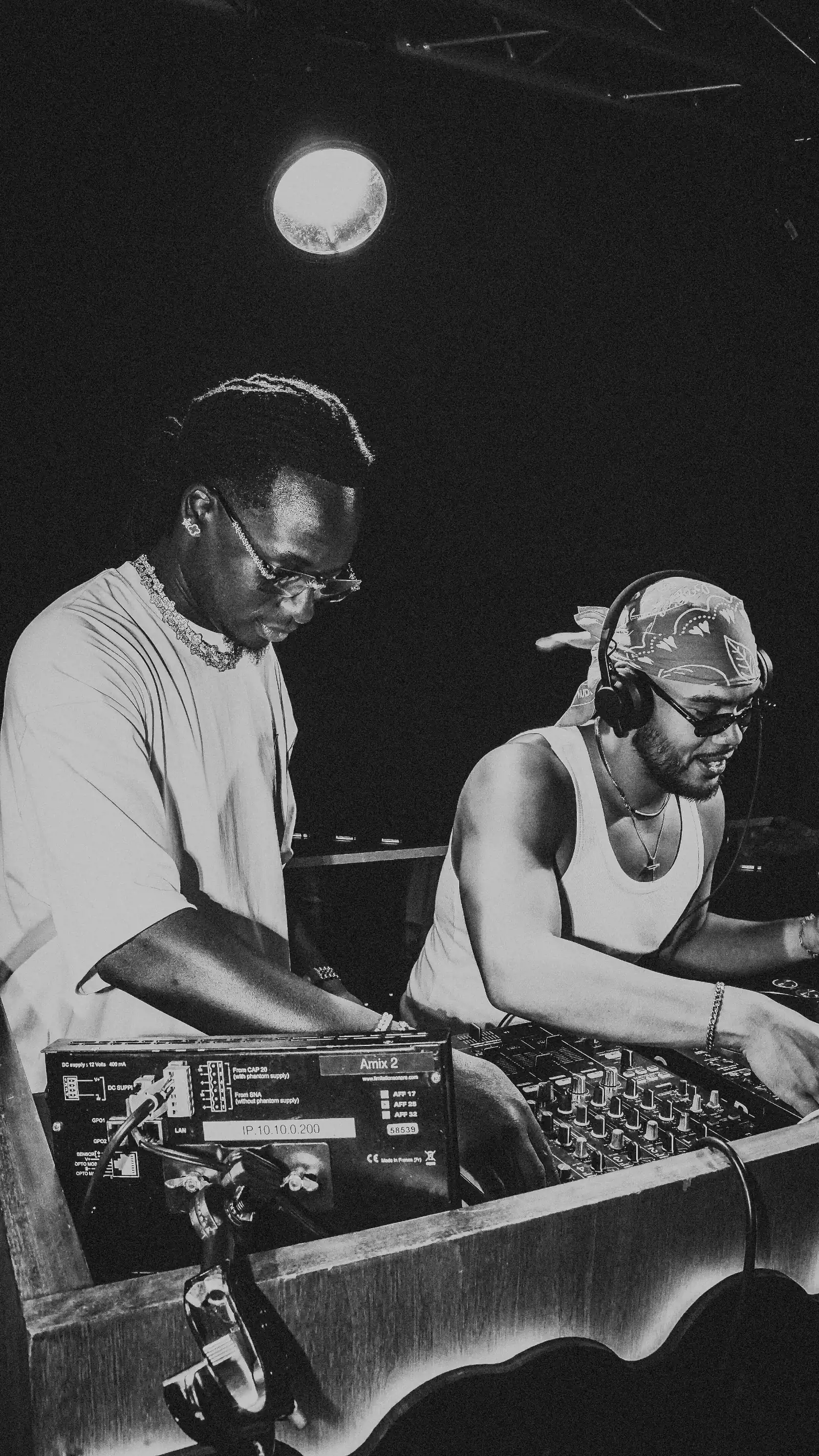 Deux DJ hommes mixant de la musique sur platines dans un club sombre, noir et blanc.